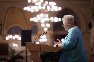 Side view of Ulli Felt during her lecture, with lights in the background