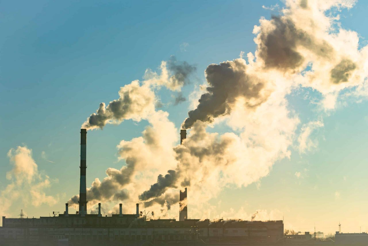 Industrial facility with multiple smokestacks emitting thick smoke into a clear blue sky.