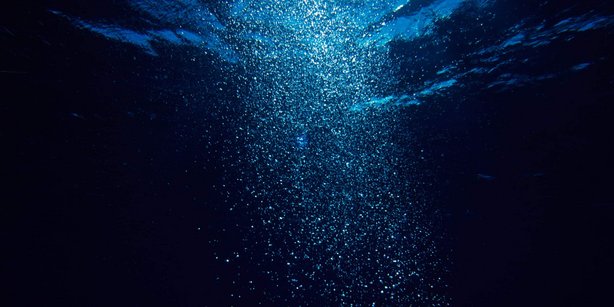 Underwater scene with air bubbles rising toward the surface, illuminated by light from above against a dark blue background.