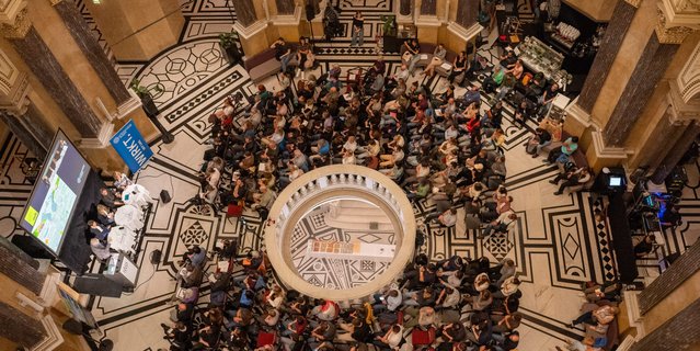 Blick von oben auf das Event „Umwelt im Gespräch 12“ in der Kuppelhalle des Naturhistorischen Museums Wien mit Bühne, Publikum und Präsentation.