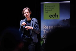 Sabine Pahl addressing the room from stage with a microphone in one hand and the ech banner in the background