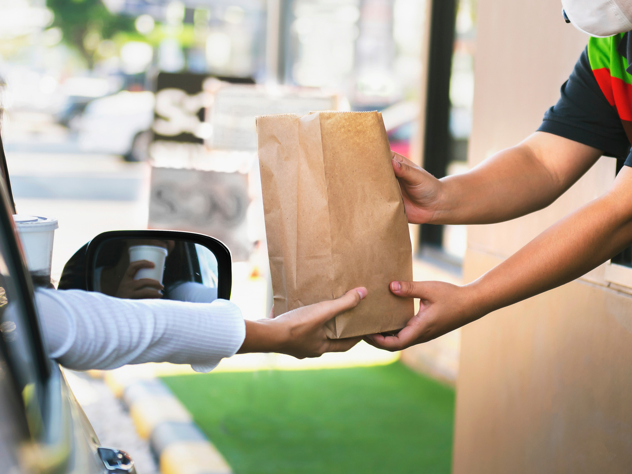A worker handing a bag of fast food to a person in a drive through