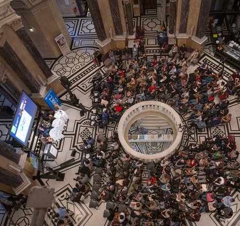 Große Menschenmenge in der Kuppelhalle des Naturhistorischen Museums, mit Bühne und Bildschirm für Präsentationen.