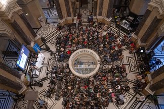 Große Menschenmenge in der Kuppelhalle des Naturhistorischen Museums, mit Bühne und Bildschirm für Präsentationen.