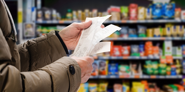 A person holding their bills in a supermarket with shelfs in the background