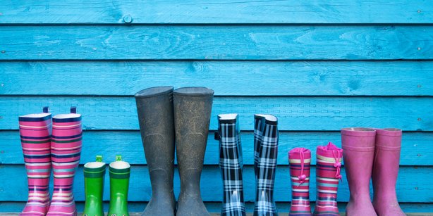 6 pairs of rubber boots in different sizes lined up next to each other in front of a bright blue wooden wall