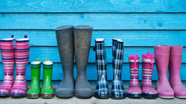 6 pairs of rubber boots in different sizes lined up next to each other in front of a bright blue wooden wall