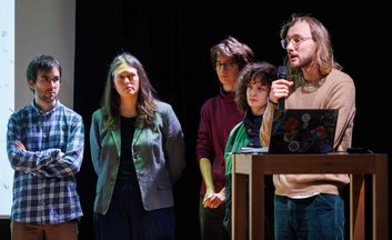 A team member presenting his team's idea, with the rest of the team standing in the background