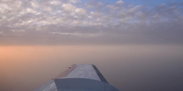 Picture of a wing of an airplane. A stratocumulus cloud layer in the background, lit by the sunset.