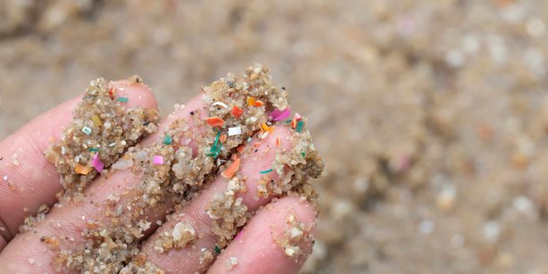 Hand holding sand mixed with small colorful plastic pieces, highlighting plastic pollution.