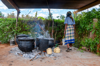 A woman standing viewed from behind next to a open fire cooking station