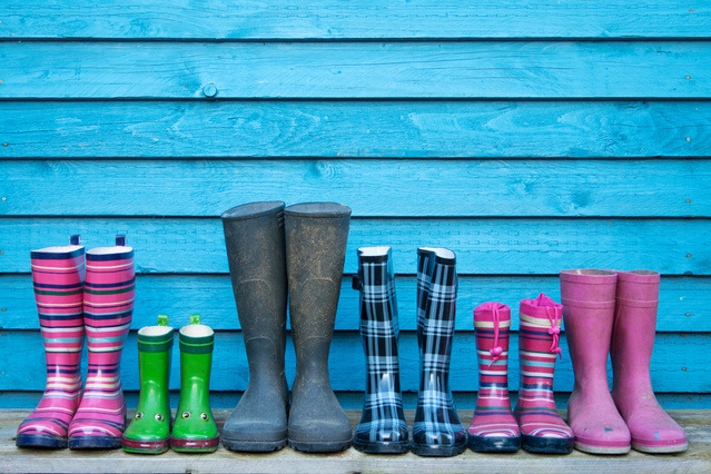 6 pairs of rubber boots in different sizes lined up next to each other in front of a bright blue wooden wall