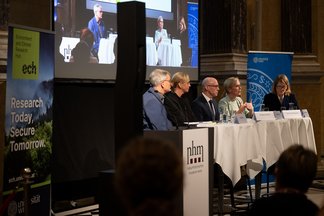 Diagonal view of the panel members with a screen in the bakcground and and ECH banner next to them
