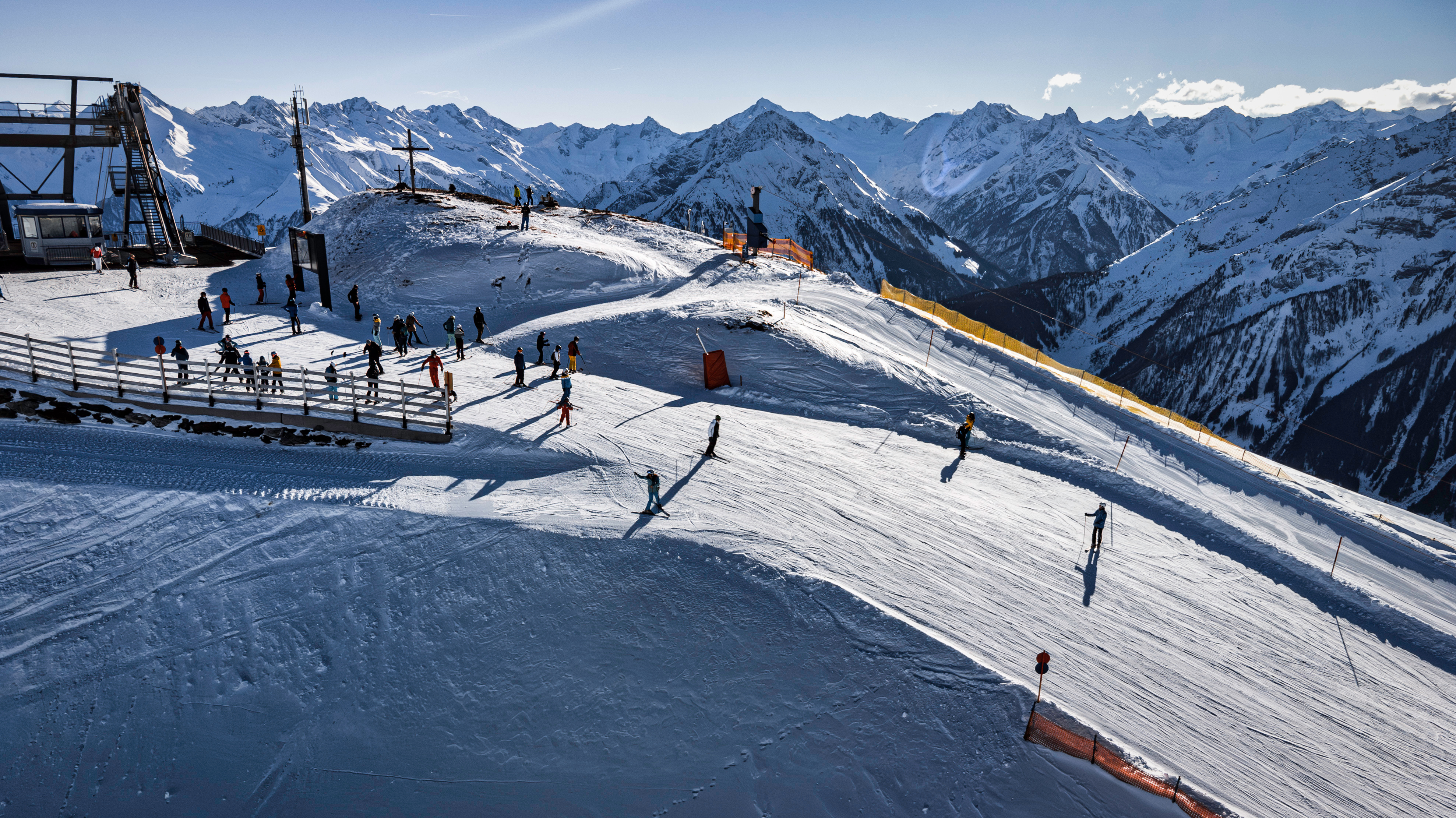 View of a mountains peak with skiiers emptying out of a lift, the alps in the background. full of snow