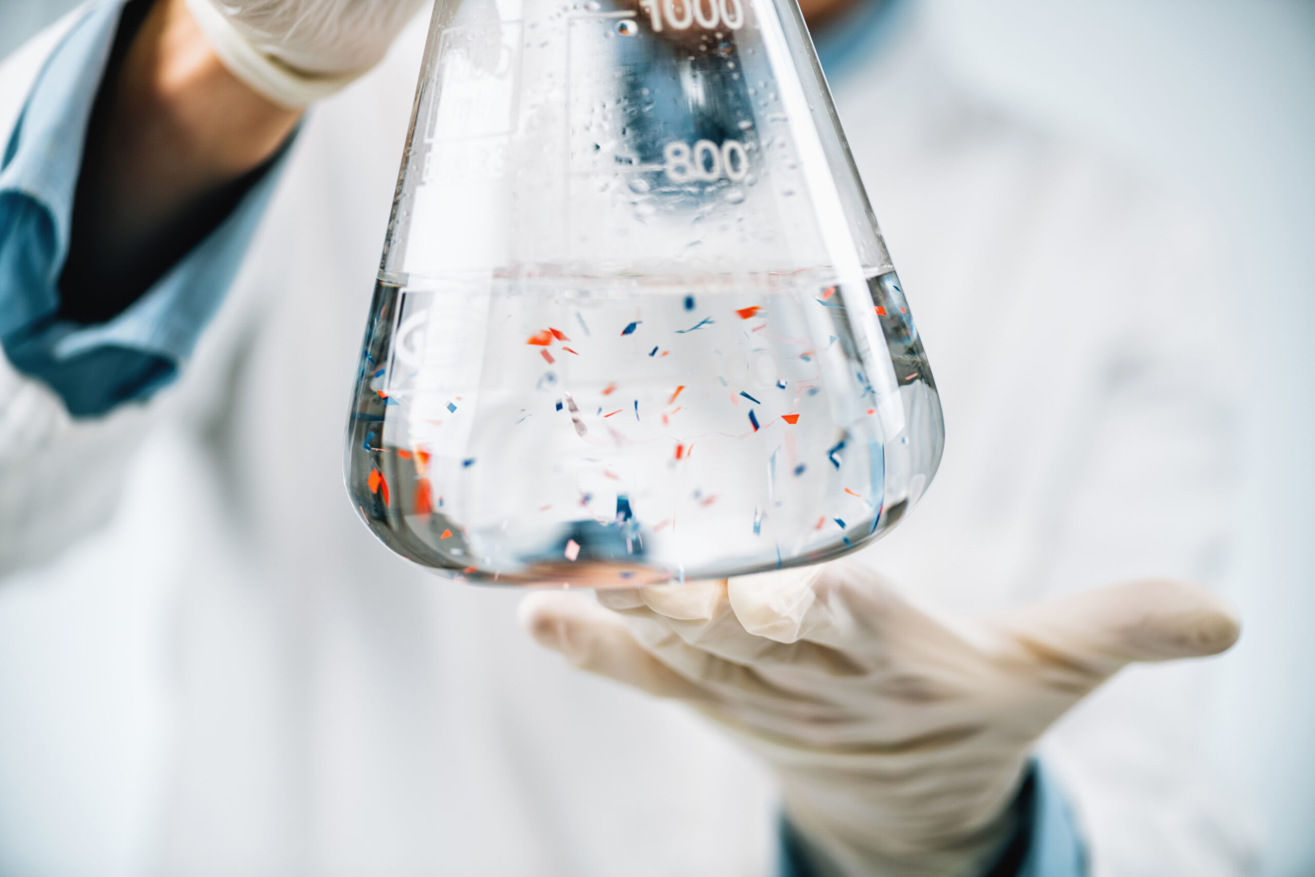 Microplastics laboratory analysis. Scientist observing microplastics or tiny plastic particles in a flask with a water sample.